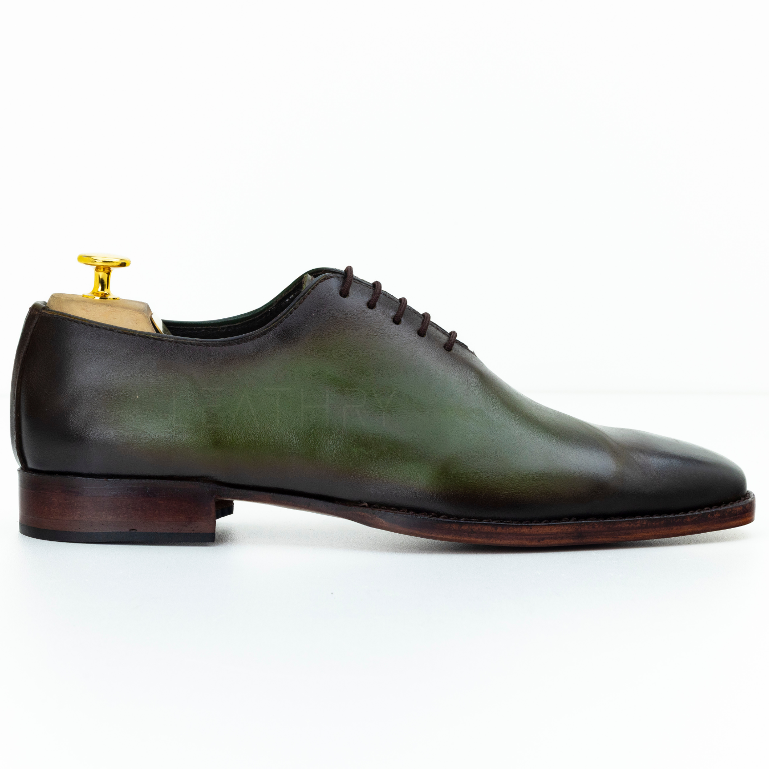 Green leather dress shoe with brown sole on a white background