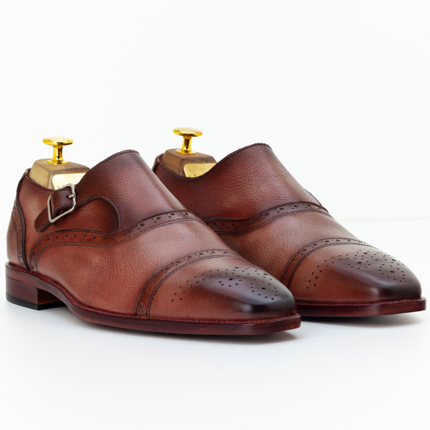 Pair of brown leather dress shoes with gold buckles on a white background