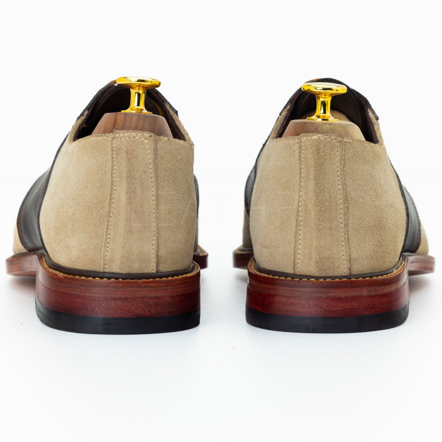 Pair of tan suede shoes with brown soles on a white background